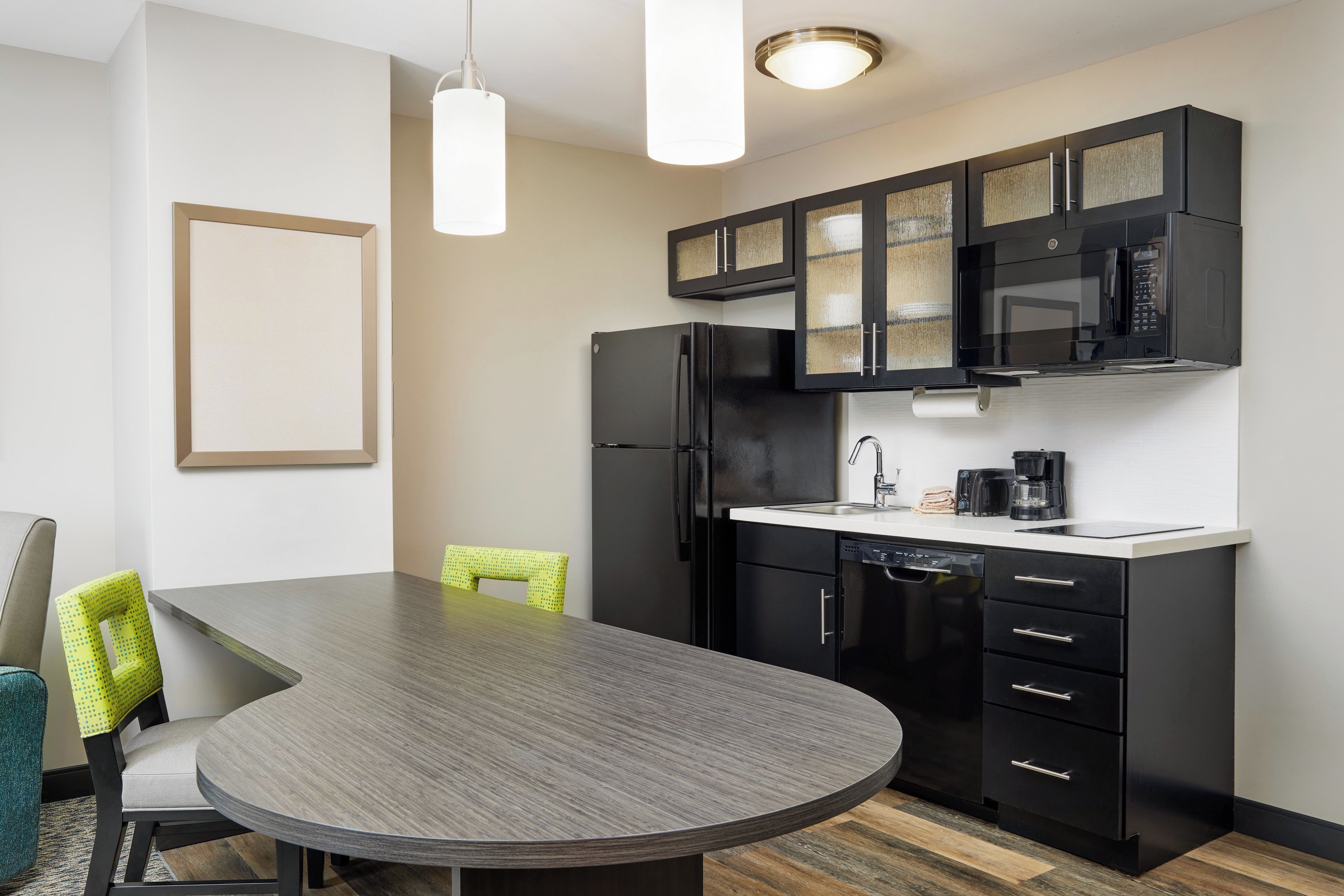 A modern kitchen with a round dining table, black cabinets, a built-in microwave, and a coffee maker.