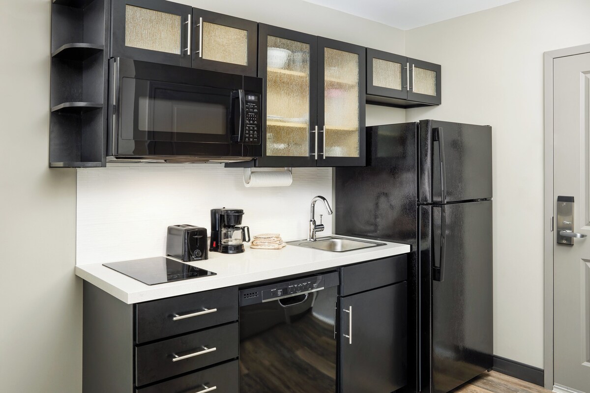 Una cocina moderna con armarios negros, un refrigerador de acero inoxidable, microondas, cafetera y lavavajillas.