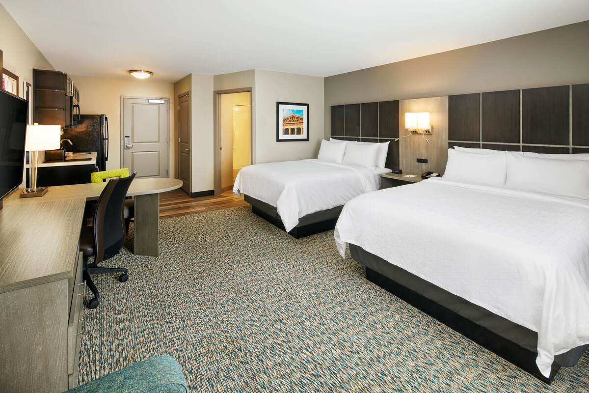 A hotel room with two beds, a desk with a chair, a small table, and a TV.