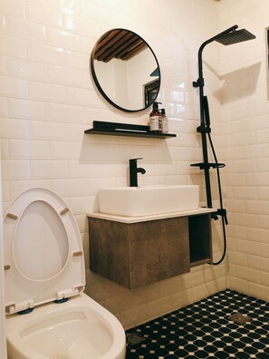 A bathroom with a toilet, sink, mirror, shower, and tiled floor. - Back Home (Tainan)