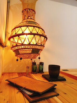 A traditional woven lamp, a wooden table, a notebook, and two glass bottles. - Back Home (Tainan)