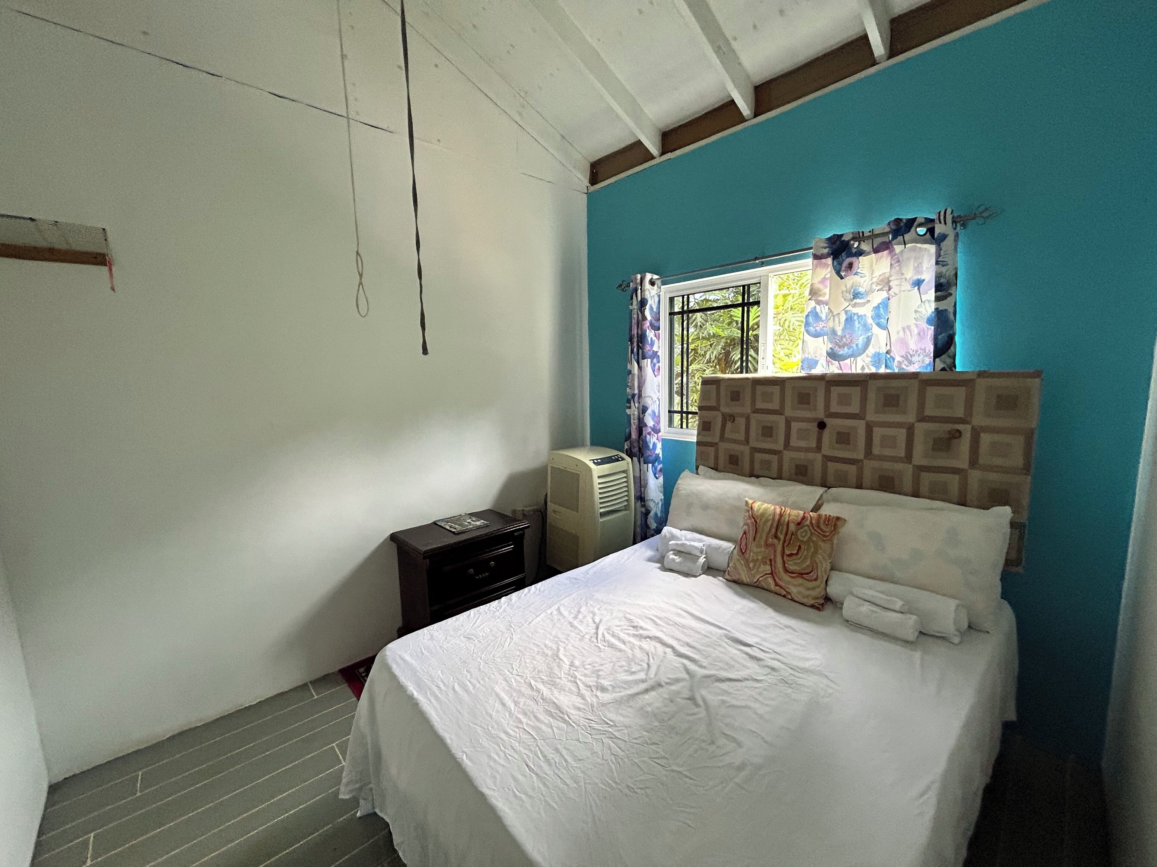 Un dormitorio con cama, mesita de noche, ventana con cortinas y radiador.