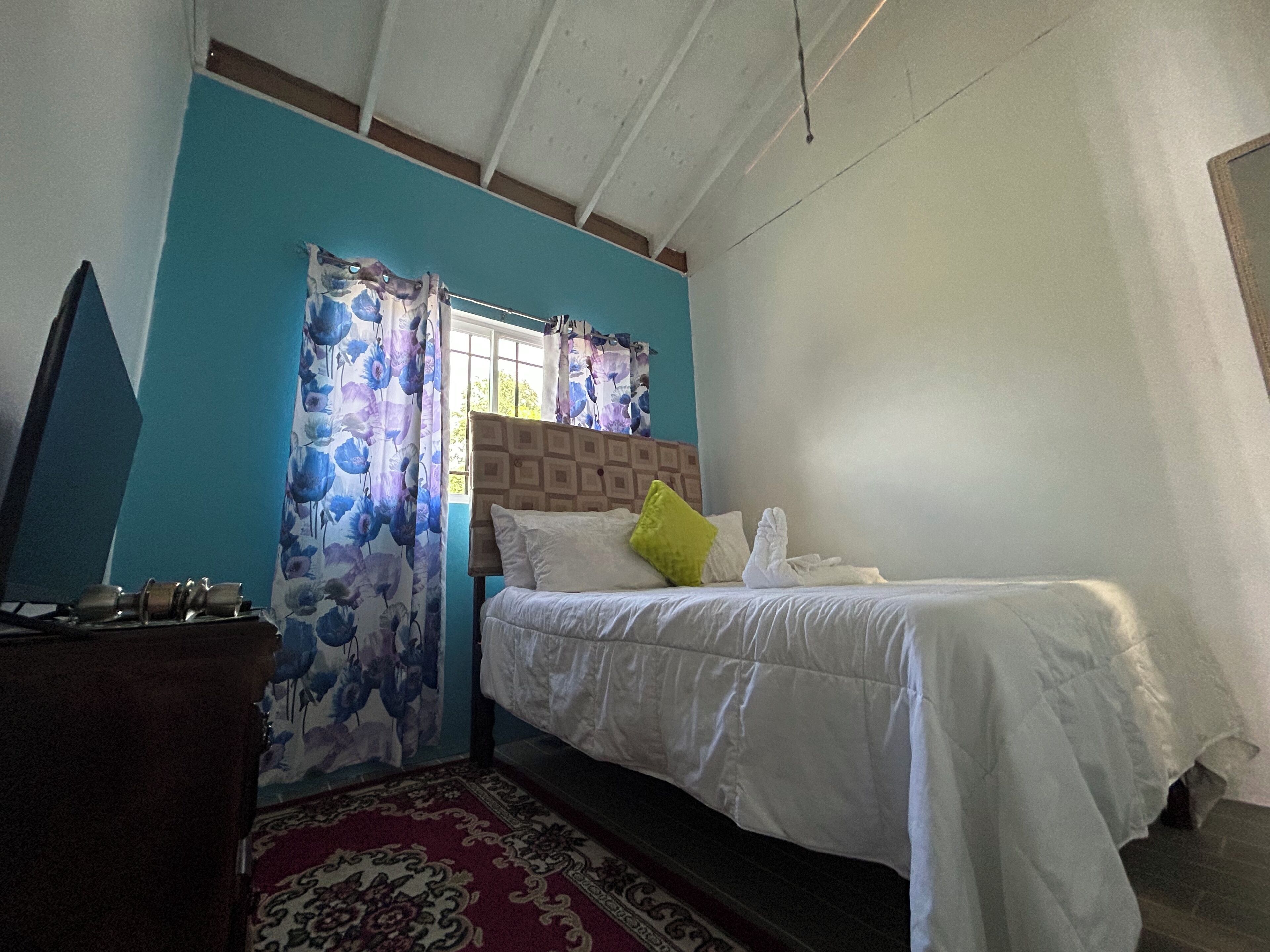 Een slaapkamer met een bed, gordijnen en een televisie.