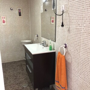 Casa de banho com lavatório branco, armário escuro e porta-toalhas com toalha laranja.