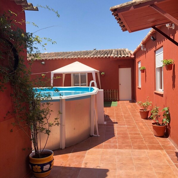 Piscina com toldo, cercada por paredes vermelhas e plantas em vasos.