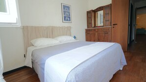 Een slaapkamer met een bed, een houten garderobe, een raam met gordijnen en een ingelijste foto aan de muur.
