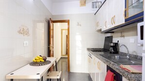 Una cocina compacta con paredes de azulejos blancos, encimera de granito y pileta de acero inoxidable.