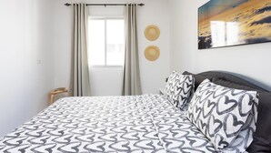 Un dormitorio con cama, ventana con cortinas, un sombrero colgado en la pared y un cuadro.
