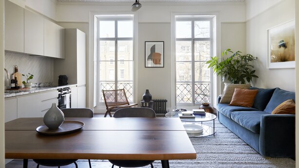 Eine moderne Küche mit weißen Schränken, einem Esstisch mit einer Vase und einem blauen Sofa mit Kissen.