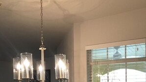 A dining area with a chandelier, a TV, and a window with blinds.