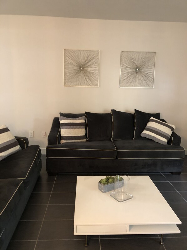 A modern living room with a black sofa set, two abstract wall art pieces, and a white coffee table with a plant.