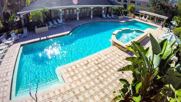 A rectangular swimming pool with a small hot tub, surrounded by lounge chairs and a covered patio area.