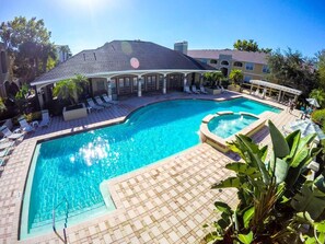 A rectangular swimming pool with a small hot tub, surrounded by lounge chairs and a covered patio area.