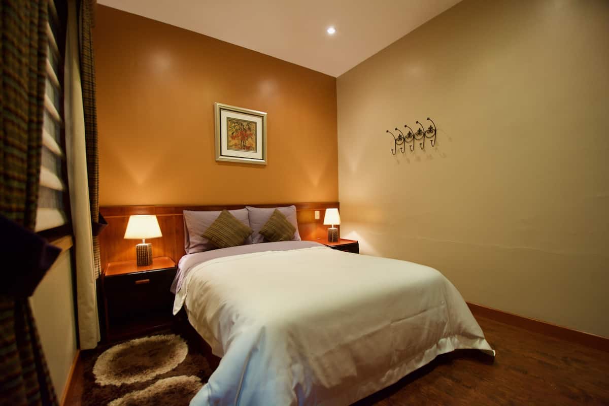 A neatly made bed with white linens, two bedside lamps, a framed picture on the wall, and a small rug on the floor.