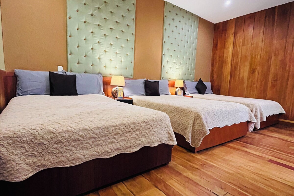 Habitación de hotel con dos camas, suelo de madera y cabecero tapizado en verde.