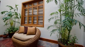 A cozy room with a wicker sofa, a large window, and several potted plants.