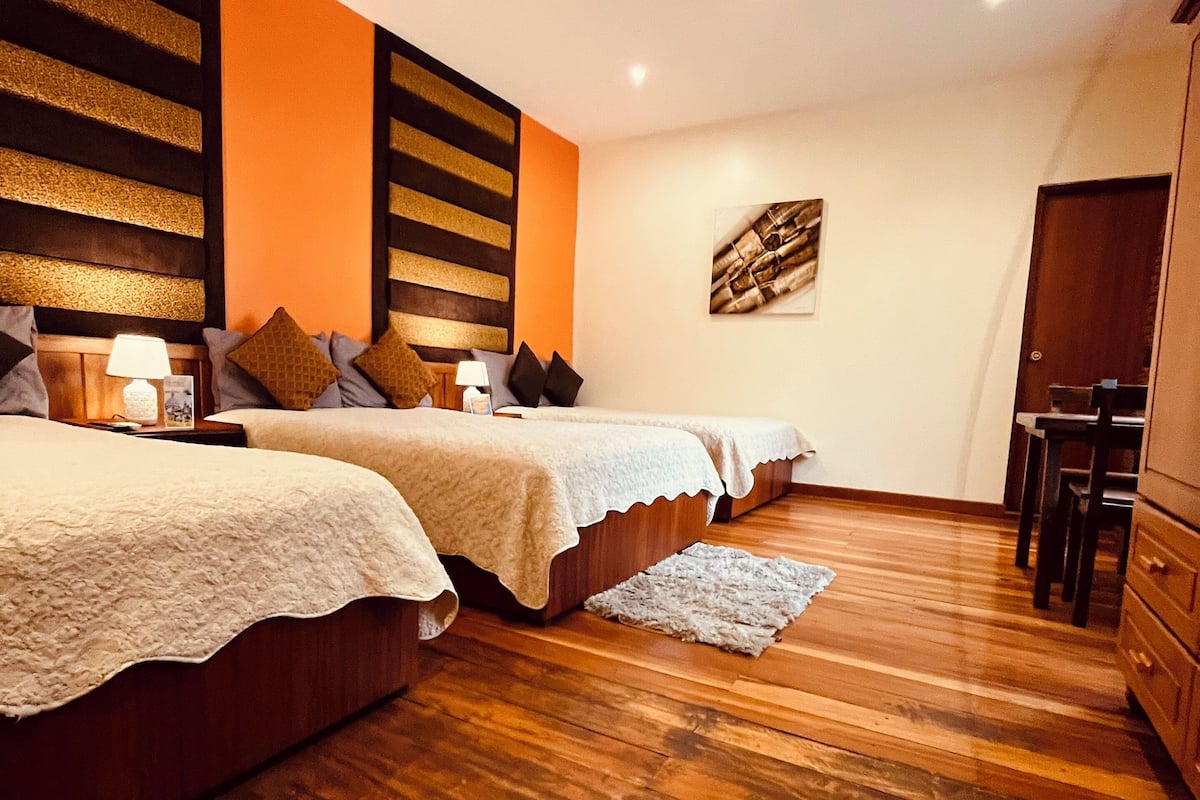 A bedroom with two beds, wooden flooring, and a small desk area.