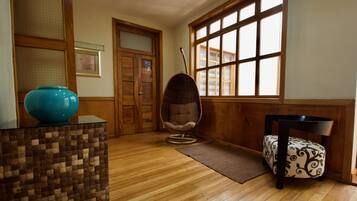 Une pièce avec un plancher en bois, une grande fenêtre, un fauteuil suspendu, un fauteuil à motifs et un vase bleu posé sur une table.