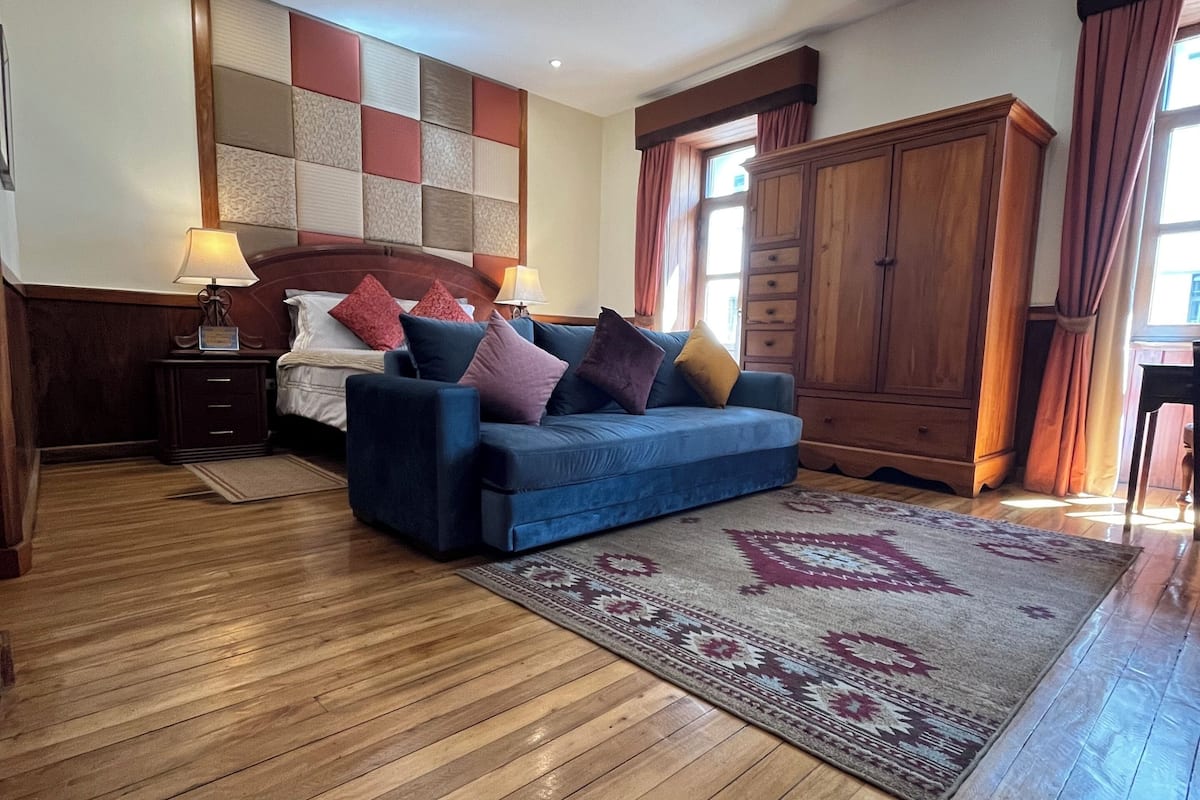 A room with a blue sofa, wooden floor, and a patterned rug.