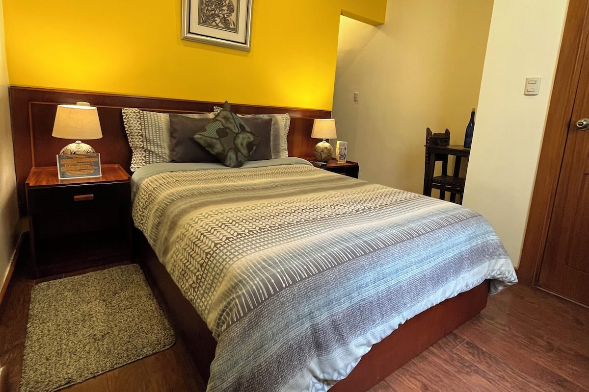A bedroom with a bed, two nightstands, a wooden headboard, a framed picture, and a wooden door.