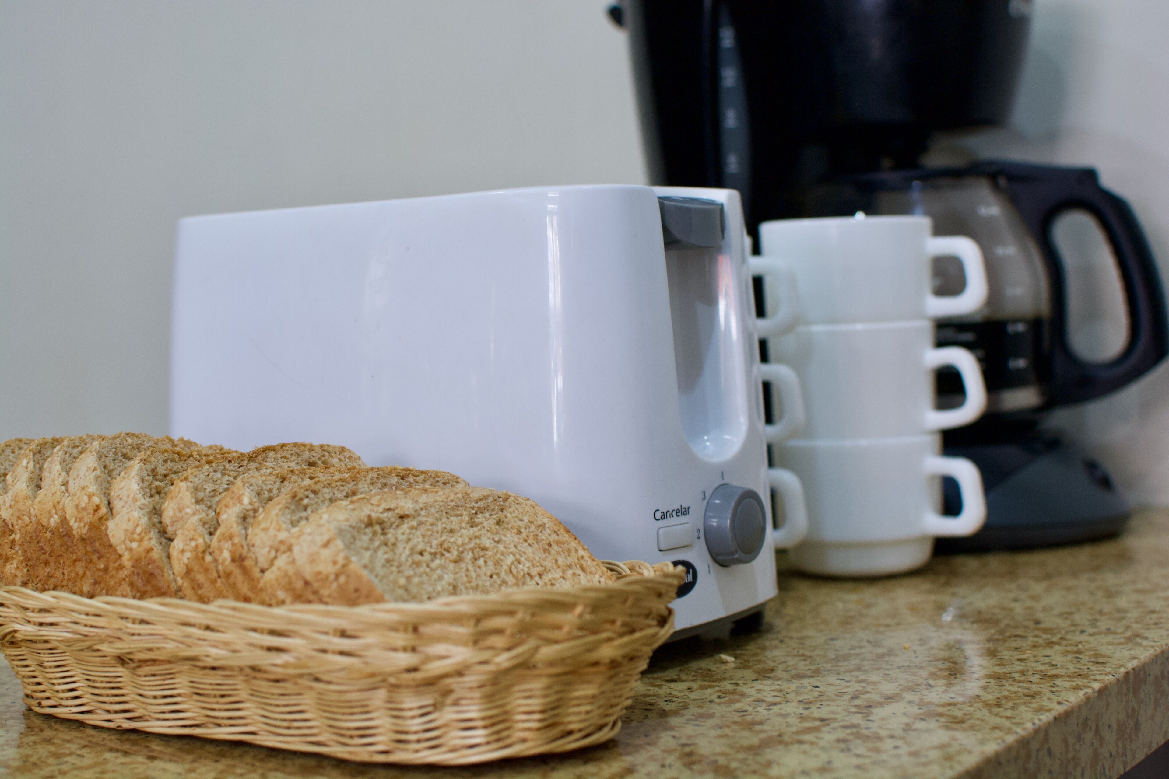 A kitchen counter with a toaster, a basket of sliced bread, and a stack of white mugs.