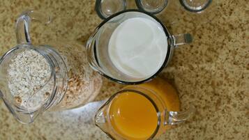 Een keukenblad met drie glazen potten: een karaf sinaasappelsap, een karaf melk en een pot havermout.