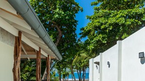 Un camino conduce a un edificio de fachada blanca, rodeado de vegetación tropical y un cielo azul claro.