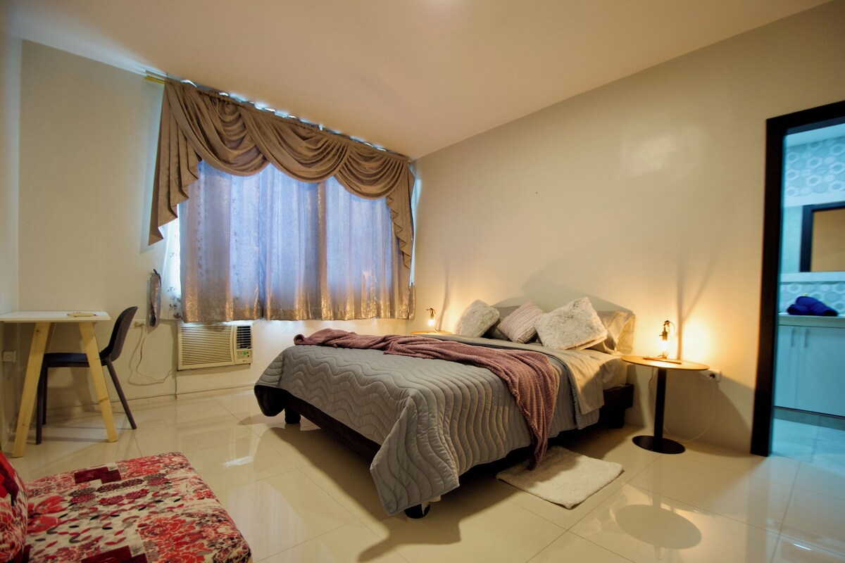 A bedroom with a bed, bedside table, lamp, and a desk with chair.