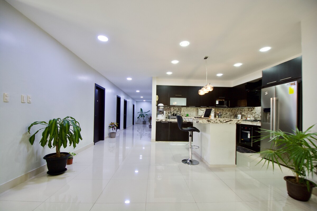 A modern kitchen with a central island, black cabinets, and stainless steel appliances.