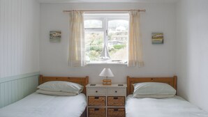 A bedroom with two single beds, a nightstand with a lamp, and a window with curtains.