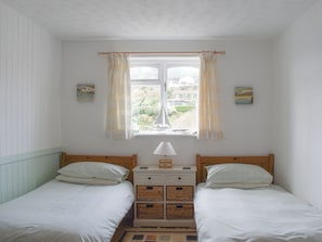 A bedroom with two single beds, a nightstand with a lamp, and a window with curtains.