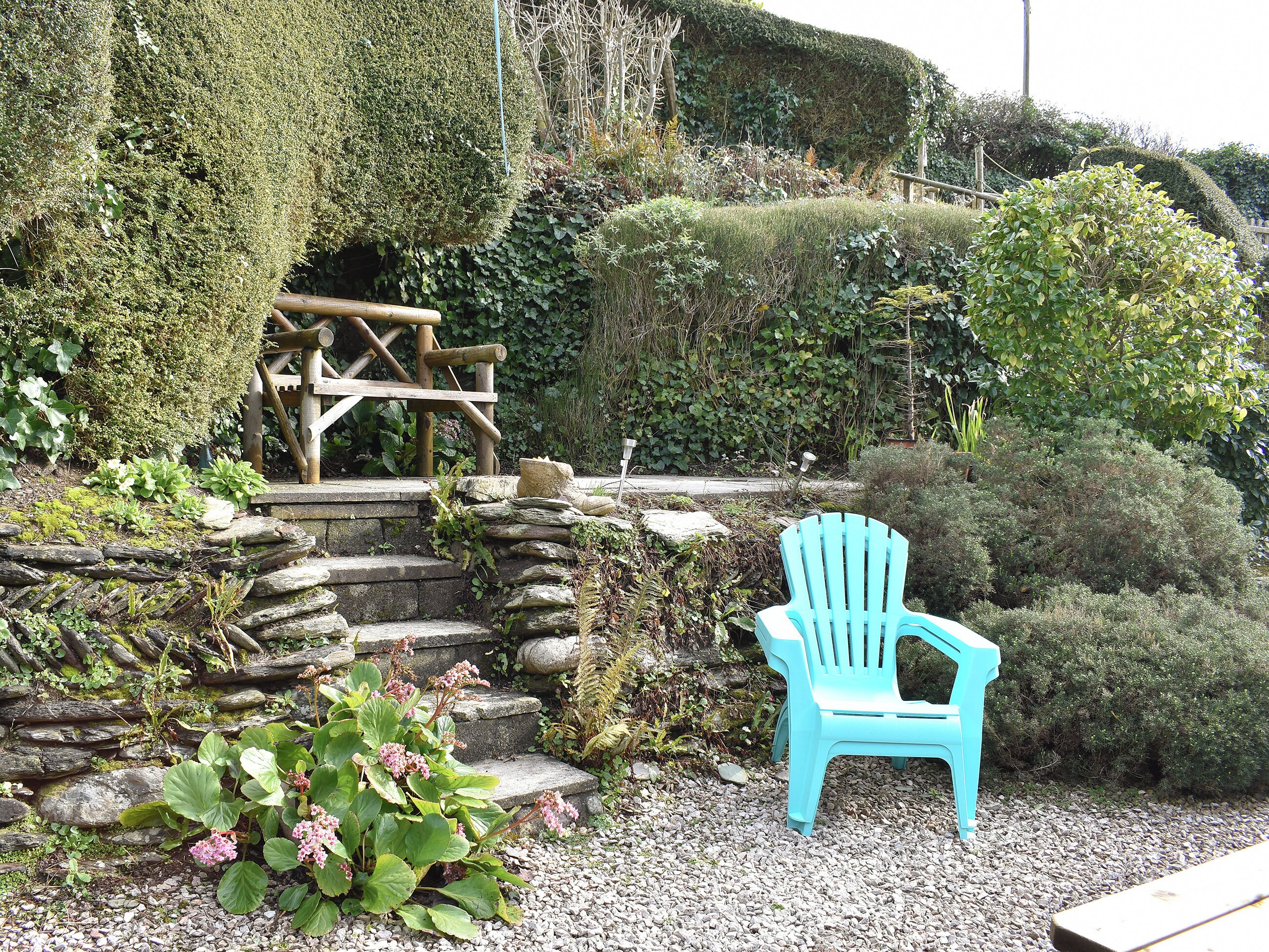 Een tuin met een houten bankje, een stenen muur en diverse planten.