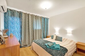 Une chambre à coucher avec un lit, des tables de chevet, un bureau et des rideaux.