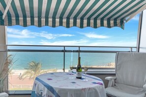 Un balcon avec vue sur la mer, une table avec une bouteille de champagne et une chaise blanche.