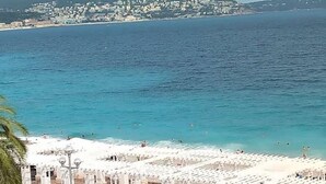 Une plage côtière bordée de parasols blancs, offrant une vue sur la mer et une ville située au loin.