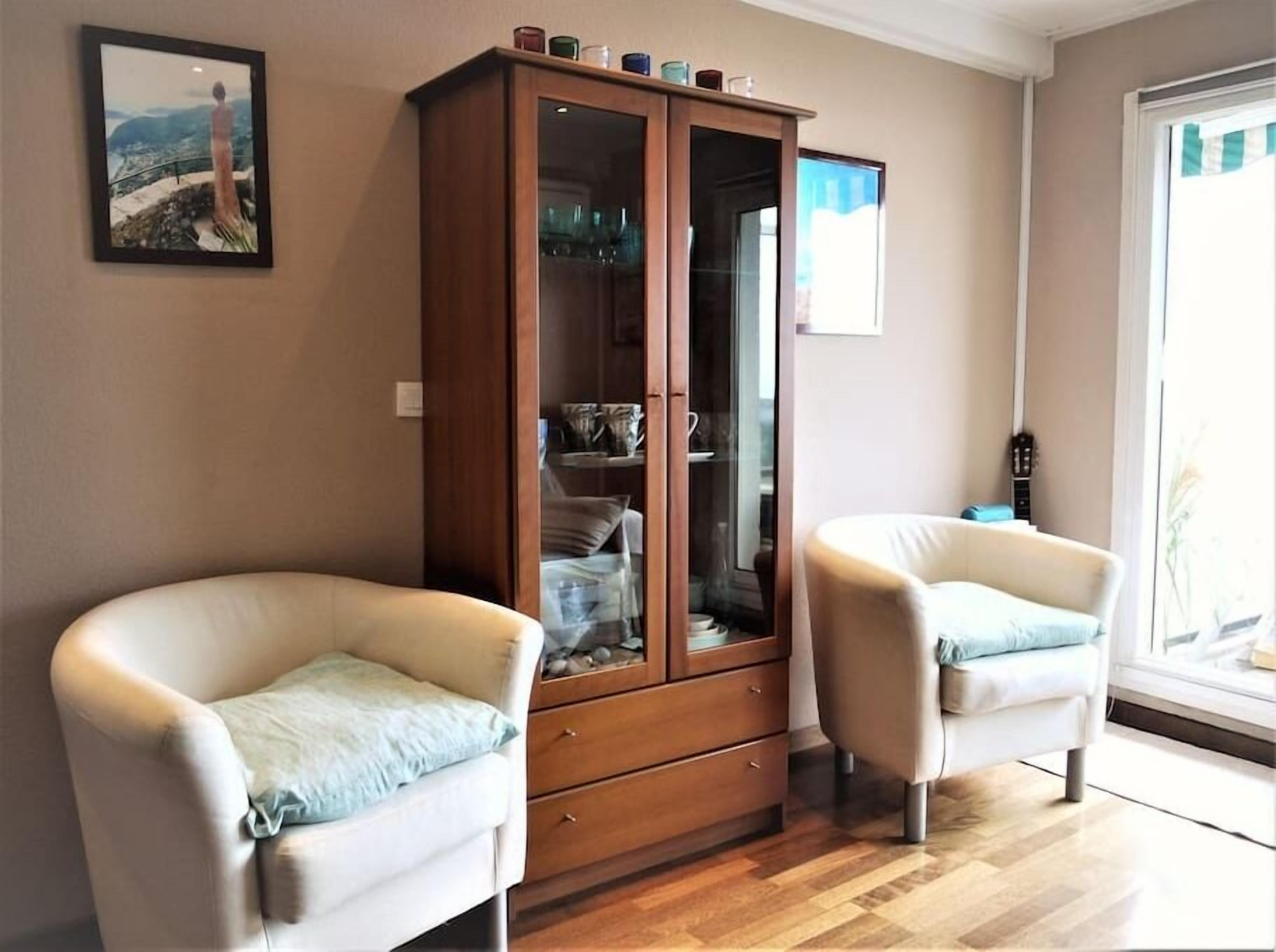 A living room with two white armchairs, a wooden cabinet, and a framed picture on the wall.