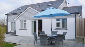 A house with a patio area featuring a table and chairs, a blue umbrella, and a view of the backyard. - 4 bedroom accommodation in Port Isaac (Port Isaac)
