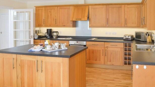 A modern kitchen with wooden cabinets, a black countertop, and stainless steel appliances. - 4 bedroom accommodation in Port Isaac (Port Isaac)