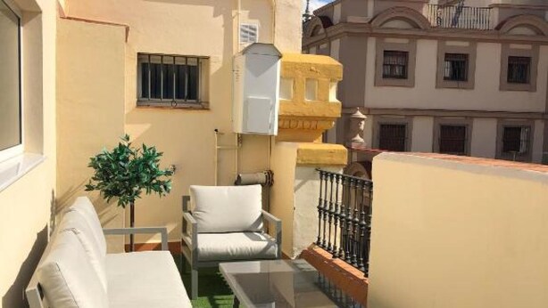 Un balcon avec un canapé et des fauteuils, une plante en pot et une rambarde.