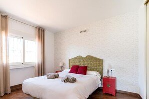 Habitación de hotel con cama, mesita de noche, lámpara y ventana con cortinas.