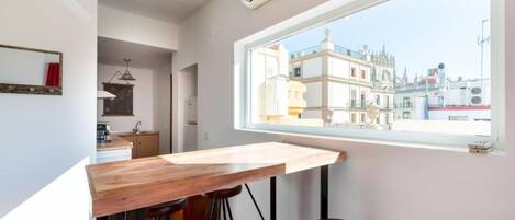 A modern kitchen with a wooden countertop and stools, a window with a city view, and an air conditioning unit.
