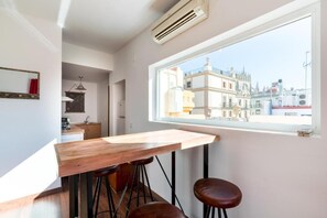 Cocina moderna con encimera de madera y taburetes, una ventana con vistas a la ciudad y un equipo de aire acondicionado.
