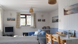 A cozy room with a bed, a TV, a sofa, a dining table with chairs, and a bookshelf. - 2 bedroom accommodation in Talland Bay, near West Looe (Talland Bay, near West Looe)