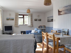 A cozy room with a bed, a TV, a sofa, a dining table with chairs, and a bookshelf.