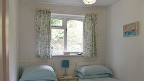 A bedroom with two single beds, a window with floral curtains, a bedside lamp, and a painting on the wall. - 2 bedroom accommodation in Talland Bay, near West Looe (Talland Bay, near West Looe)