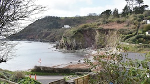 A coastal landscape with a wooden staircase leading down to a sandy beach, a cliffside, and a sign indicating a pedestrian crossing. - 2 bedroom accommodation in Talland Bay, near West Looe (Talland Bay, near West Looe)