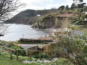 A coastal landscape with a wooden staircase leading down to a sandy beach, a cliffside, and a sign indicating a pedestrian crossing.