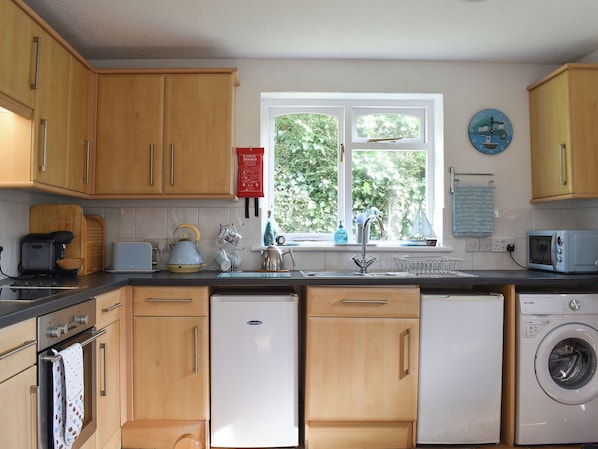 A kitchen with wooden cabinets, a washing machine, a microwave, and a window with a view of greenery.