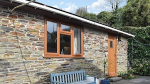 A stone house with a wooden bench in front, a door, and a window with a curtain. - 2 bedroom accommodation in Talland Bay, near West Looe (Talland Bay, near West Looe)
