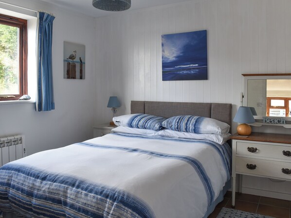 A bedroom with a bed, a nightstand, a dresser, a window with curtains, a lamp, a painting, and a radiator.
